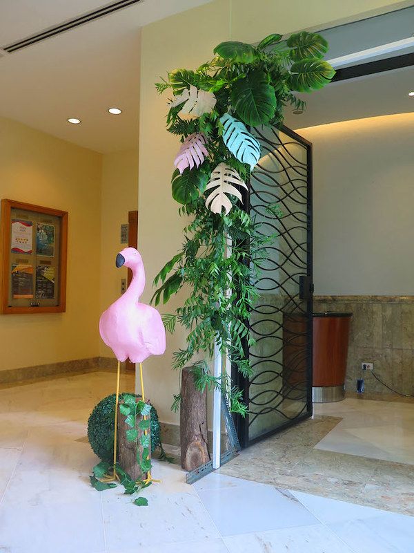 a pink flamingo statue sitting next to a tall plant in a room with white tile flooring