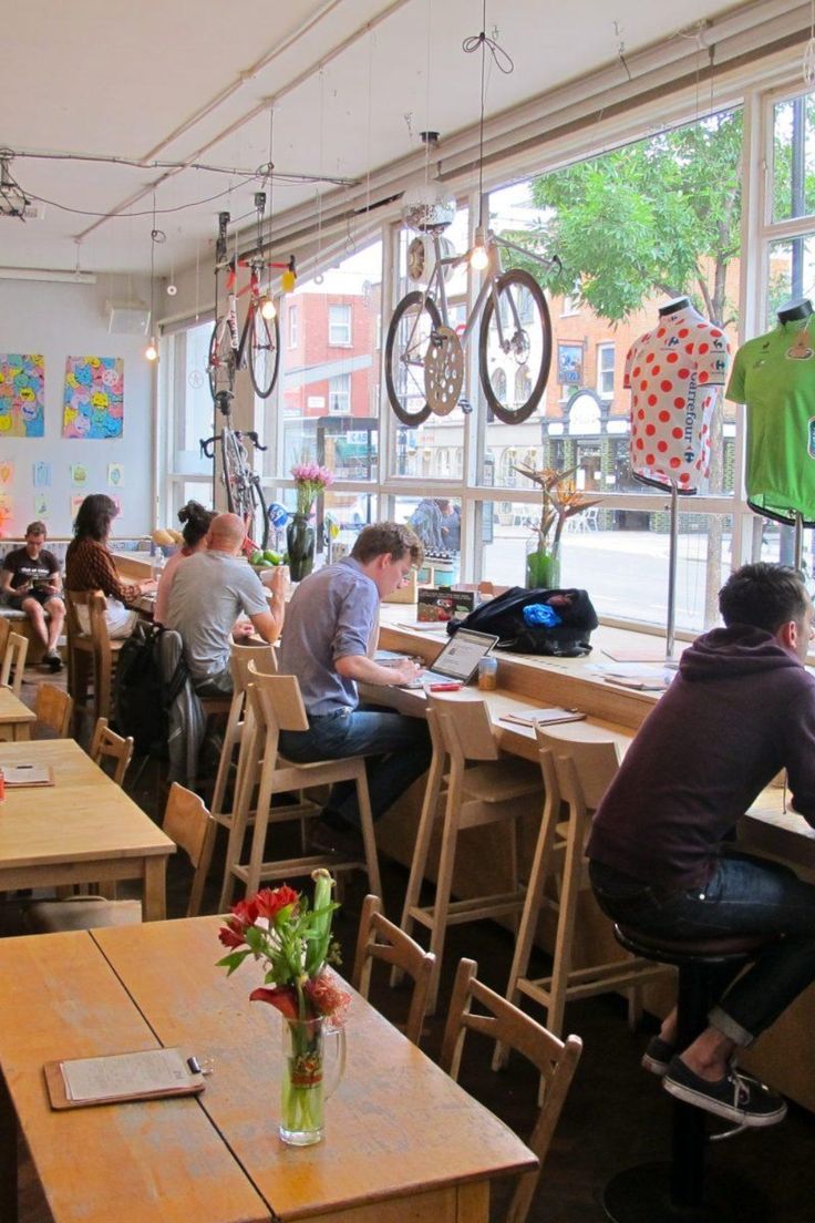 people sitting at tables in a restaurant with bicycles hanging from the ceiling and large windows