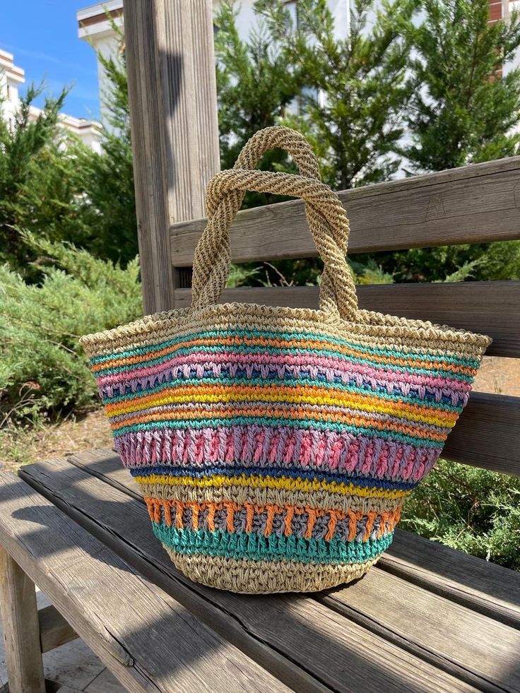 a multicolored straw bag sitting on top of a wooden bench next to trees