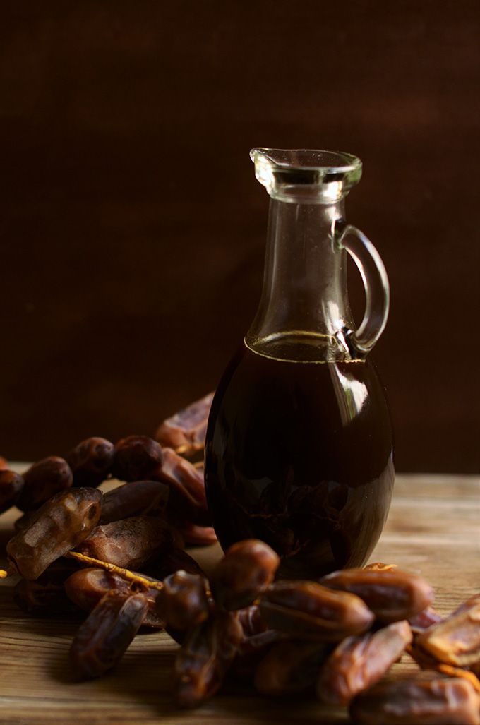 a glass bottle filled with oil sitting on top of a wooden table next to nuts