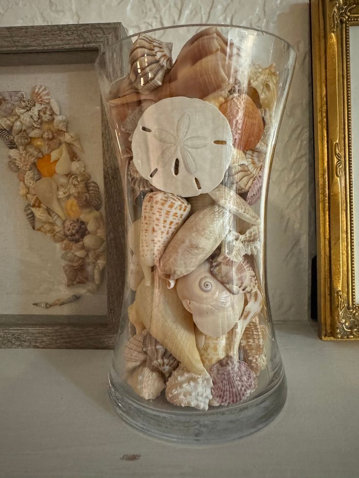 a vase filled with sea shells next to a framed picture