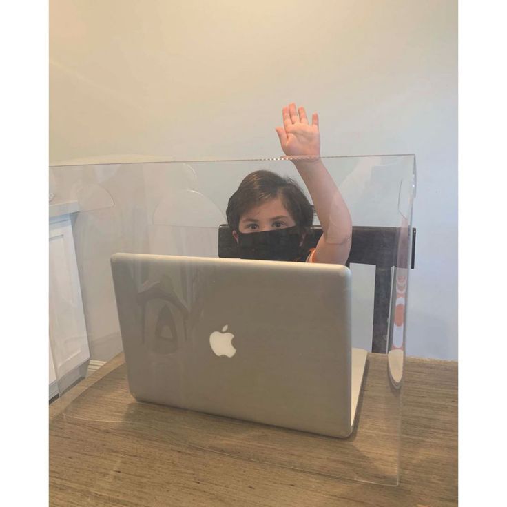 a woman sitting in front of a laptop computer with her hand up to the camera