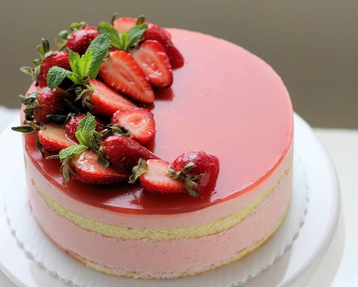 a strawberry cheesecake on a white plate topped with fresh strawberries and mint leaves