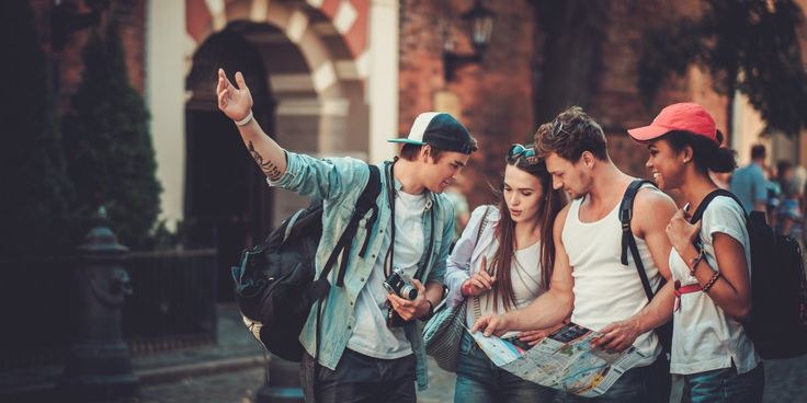 a group of young people standing around each other looking at a map and pointing to it