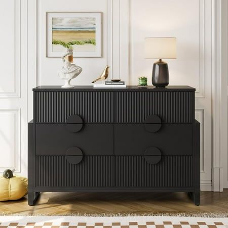 a black dresser with three drawers and a lamp on top in a white living room