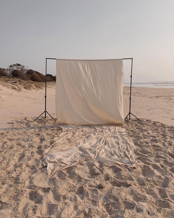 an empty photo studio set up in the sand at the beach with a white sheet draped over it