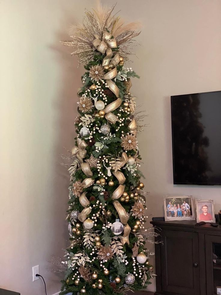 a christmas tree decorated with gold and silver ornaments in a living room next to a flat screen tv