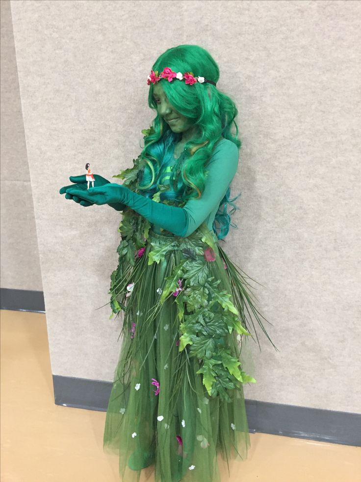 a woman dressed in green is standing next to a wall