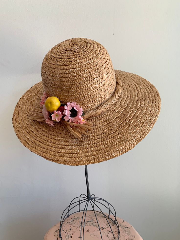 "This is a vintage 1950's straw sun hat. The hat is intricately woven with a braided section across the brim. There is also pink tone faux floral details. By the faux flowers there are also plastic faux fruit adding a pop of color and texture. The hat is in excellent condition. Measurements: Circumference: 21\" | Inside Depth: 5.5\" | Brim Depth: 4\" | Brim Circumference: 46\" Unless otherwise stated all vintage items are used and may have minor to moderate wear or discoloration considering the Braided Natural Hat For Spring, Braided Natural Spring Hat, Spring Braided Toquilla Straw Hat, Whimsical Beach Hat For Spring, Handmade Toquilla Straw Panama Hat For Spring, Spring Braided Toquilla Straw Boater Hat, Adjustable Pink Straw Hat, Bohemian Pink Sun Hat For Garden Party, Pink Bohemian Sun Hat For Garden Party