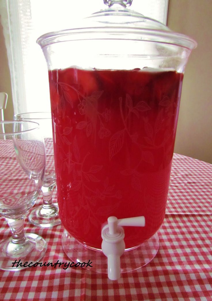 a pitcher filled with liquid sitting on top of a red checkered table cloth next to wine glasses