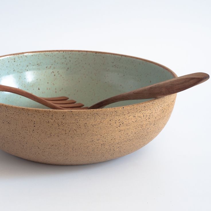 a brown and blue bowl with two wooden spoons in it on a white surface