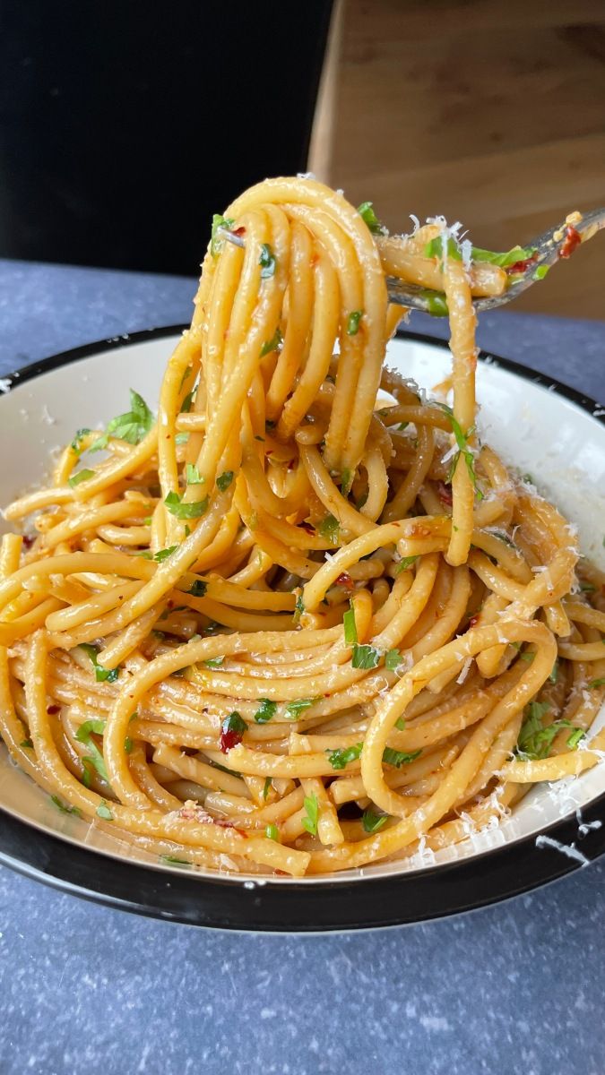 a plate full of spaghetti with parmesan cheese and herbs on top, being held by a fork