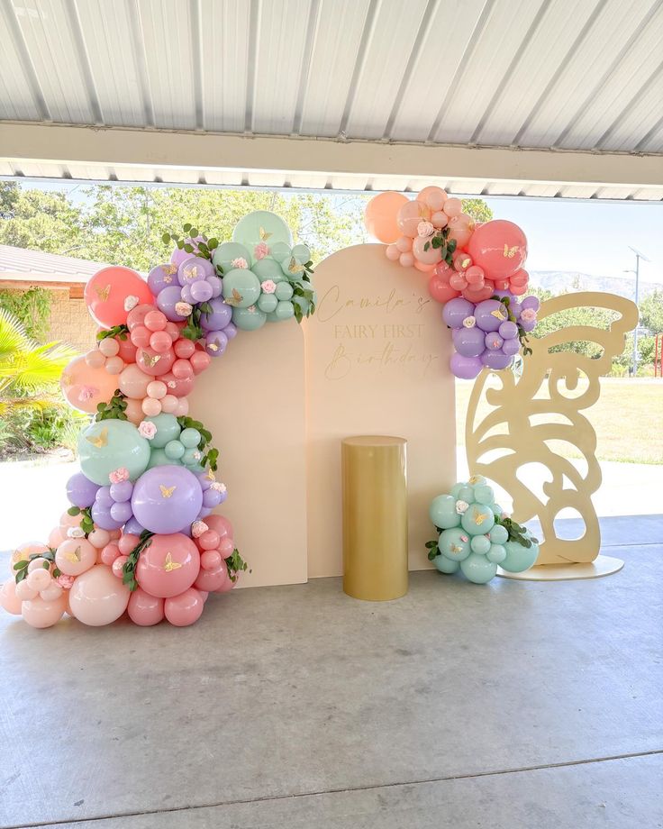 an arch with balloons and flowers on the top is decorated in pastel pinks, purples, and blue