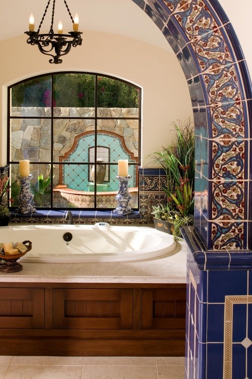 a large bath tub sitting under a window next to a chandelier with candles on it