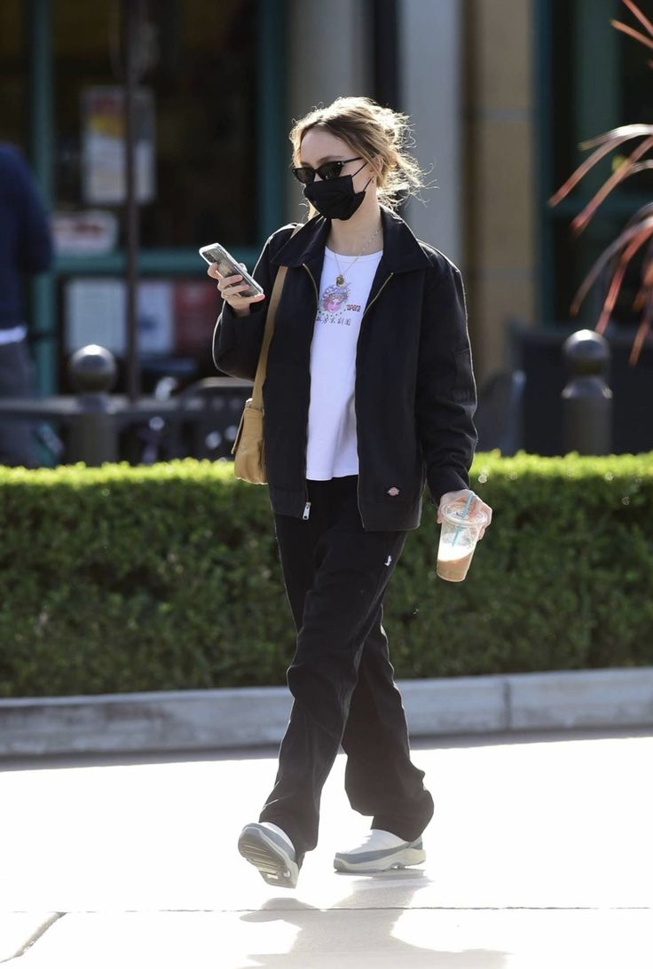 a woman wearing a face mask walks down the street while looking at her cell phone