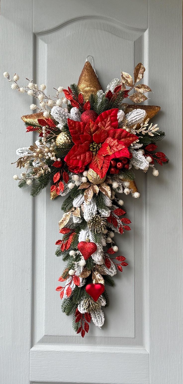 a christmas wreath on the front door with red and white flowers, pine cones, berries and bells