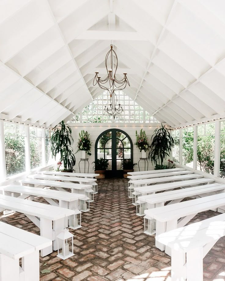 the inside of a church with white benches and potted plants on either side of the doors