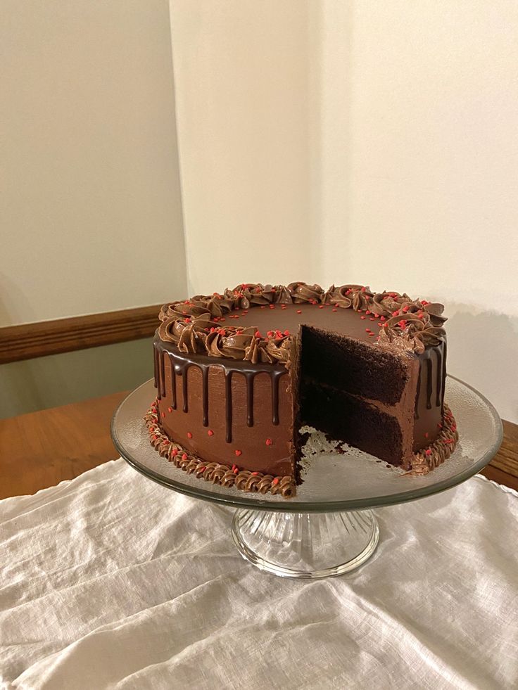 a chocolate cake sitting on top of a glass platter next to a white table cloth