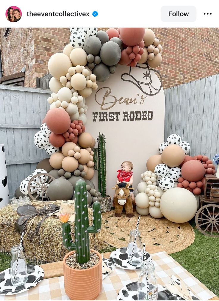 an outdoor party with balloons and cactuses on the grass, including a sign that says baby's first rodeo