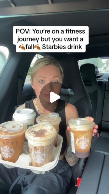 a woman sitting in the back seat of a car holding up two cups of coffee