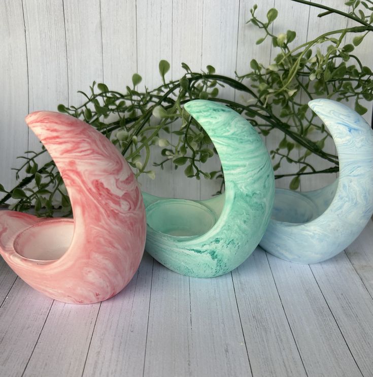 three vases sitting next to each other on a wooden floor with greenery in the background