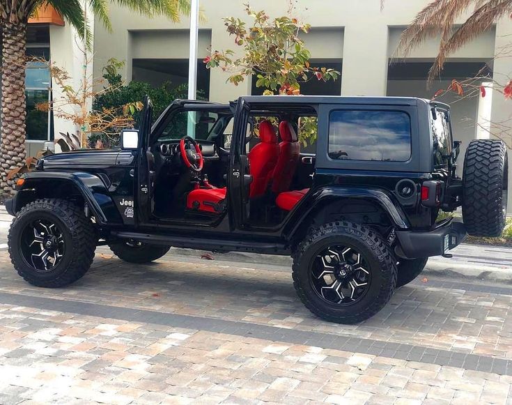 a black jeep with red leather seats is parked in front of a building and palm trees