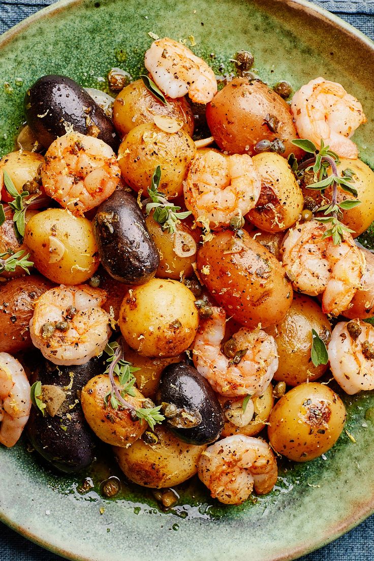 a plate filled with potatoes and shrimp on top of a blue table cloth next to a fork