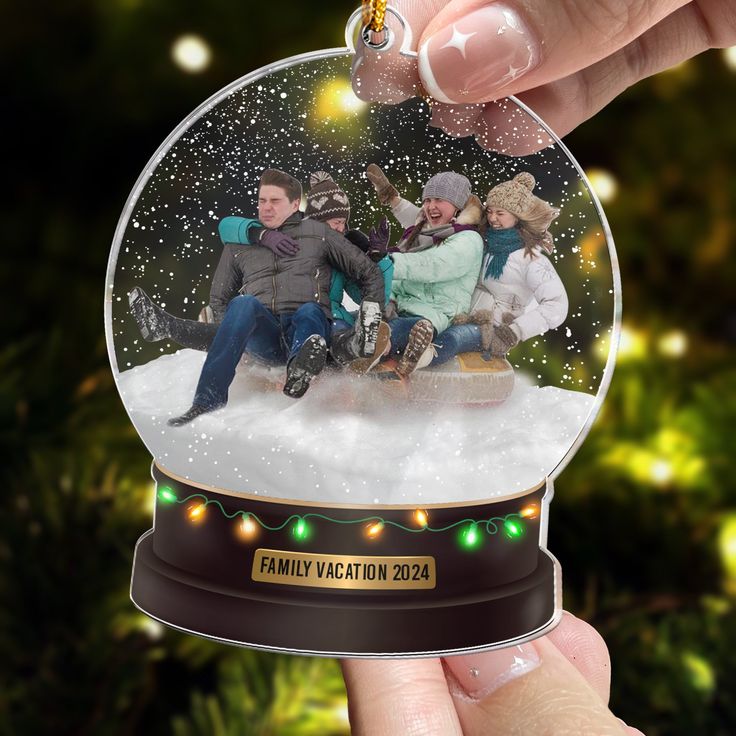 a snow globe with people sitting in it and lights on the ground around them, as well as a christmas ornament