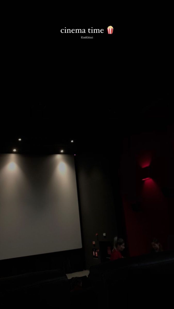 an empty screen in a dark room with red lighting on the walls and people sitting down