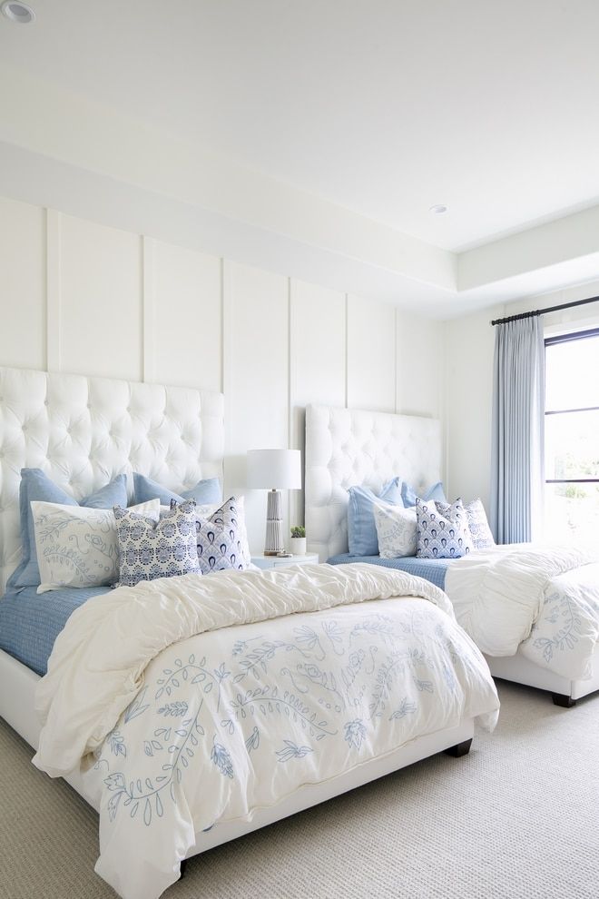 two white beds with blue and white comforters in a large, well lit bedroom