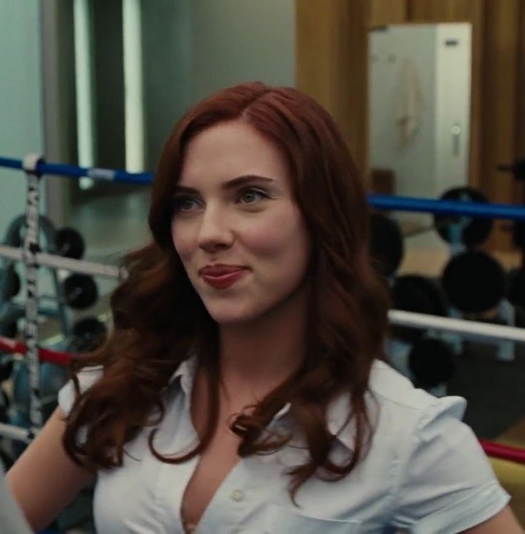 a woman with red hair is standing in front of a boxing ring and looking at the camera