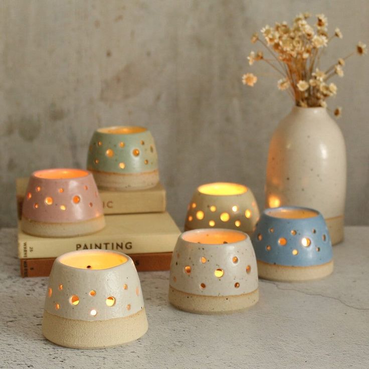 four ceramic candles are sitting next to each other on top of books and a vase with flowers in it