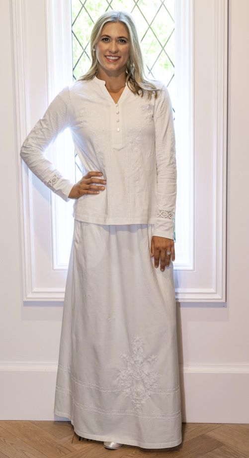 a woman standing in front of a window with her hands on her hips wearing a white dress