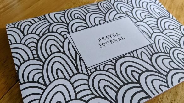 an open prayer journal sitting on top of a wooden table with black and white designs