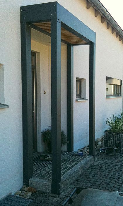 an open door to a white building next to a brick walkway and potted plants