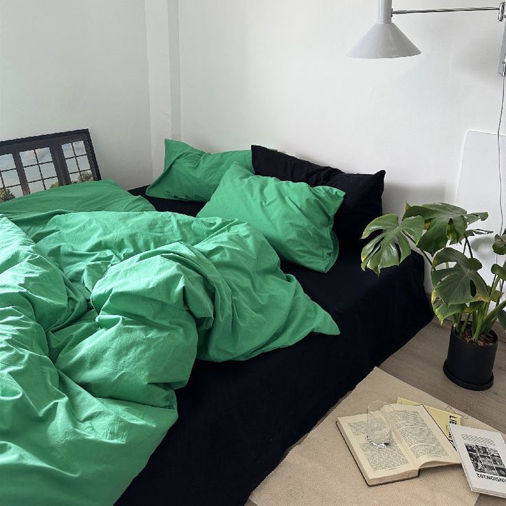 an unmade bed with black and green sheets on it, next to a potted plant