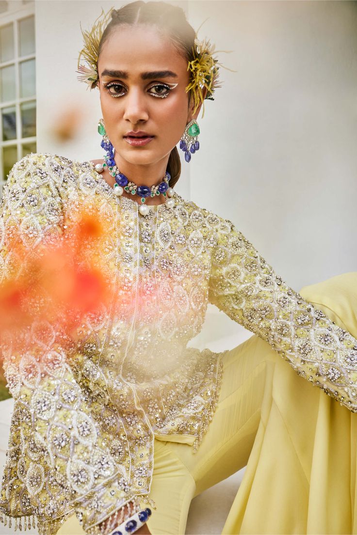 Dazzle in this exquisite set featuring a yellow and lilac jacket adorned with intricate cutdana, pearl, and sequin embroidery, accented by handmade buttons and tassels. Complete the look with chiffon sharara pants and an embroidered net dupatta for a truly regal appearance. Chiffon Sharara, Pineapple Yellow, Sharara Pants, Handmade Buttons, Personal Shopping Service, Sequin Embroidery, Yellow Jacket, Sharara Set, Net Dupatta