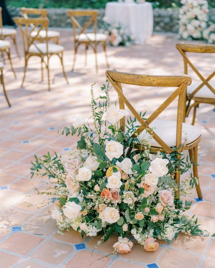 an arrangement of flowers and greenery sits on the ground in front of two chairs