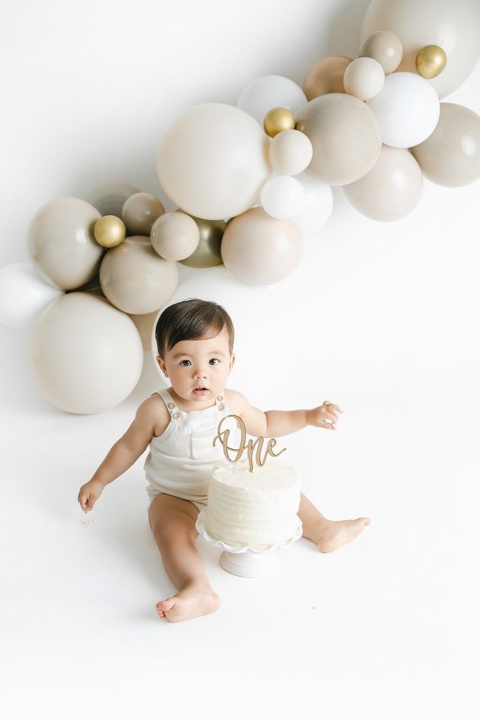 a baby is sitting in front of balloons and cake