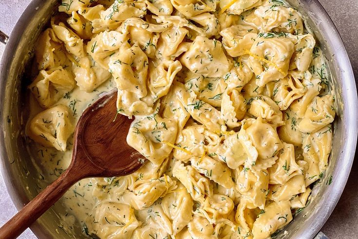 a wooden spoon in a pot filled with macaroni and cheese pasta on top of a table