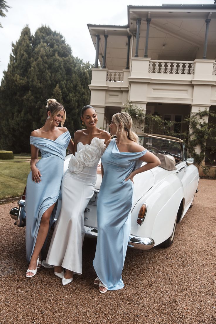 three bridesmaids pose in front of a classic car with their dresses draped over