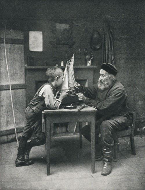 an old photo of two men sitting at a table with a paper boat in front of them