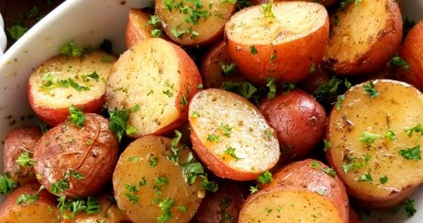 a white bowl filled with potatoes and parsley on top of a green table cloth