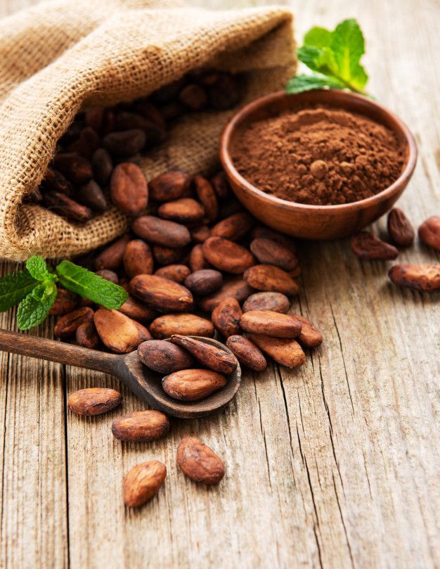 cocoa beans and powder in a sack on a wooden table with a spoon next to it