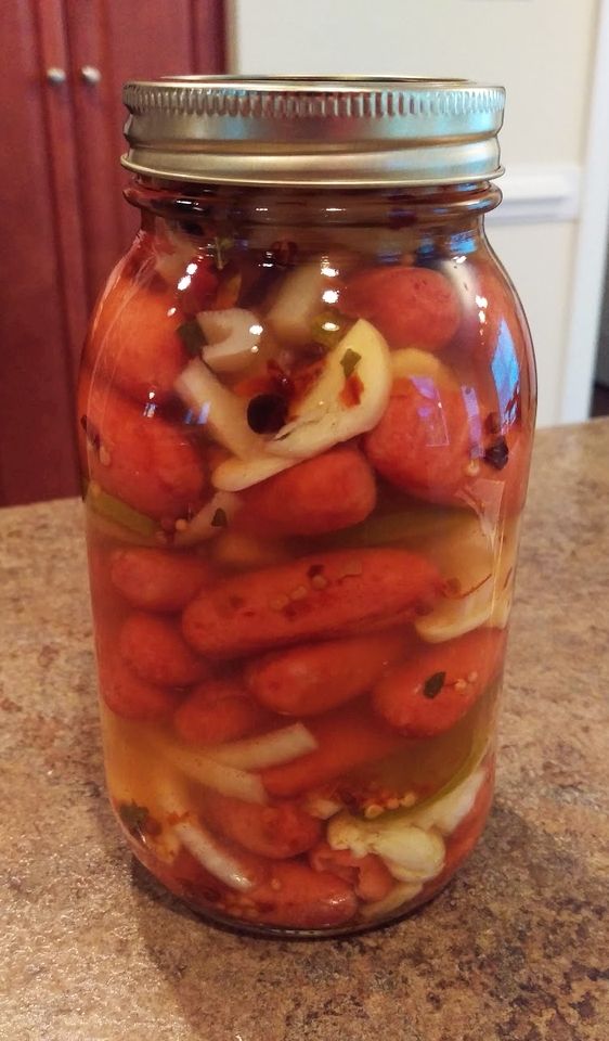 a jar filled with hot dogs and onions on top of a kitchen counter next to a refrigerator