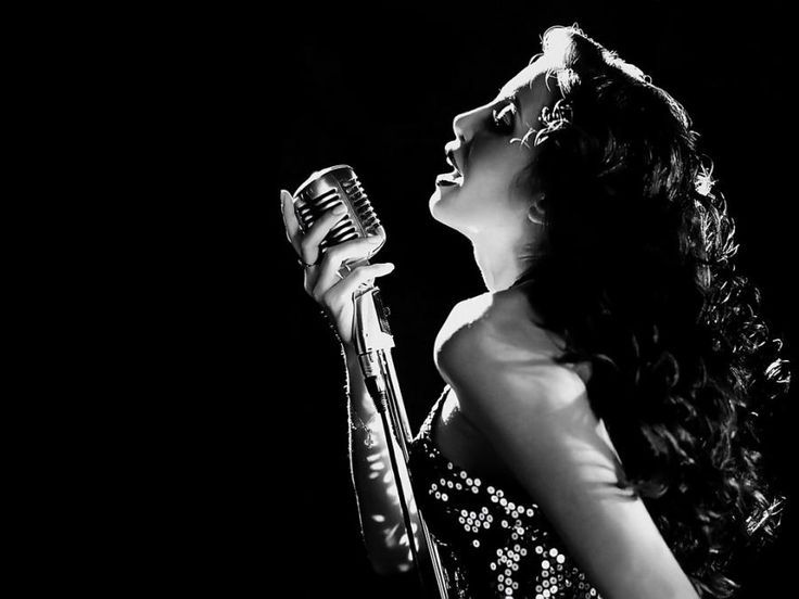 a woman holding a microphone in her right hand and singing into the microphone with both hands