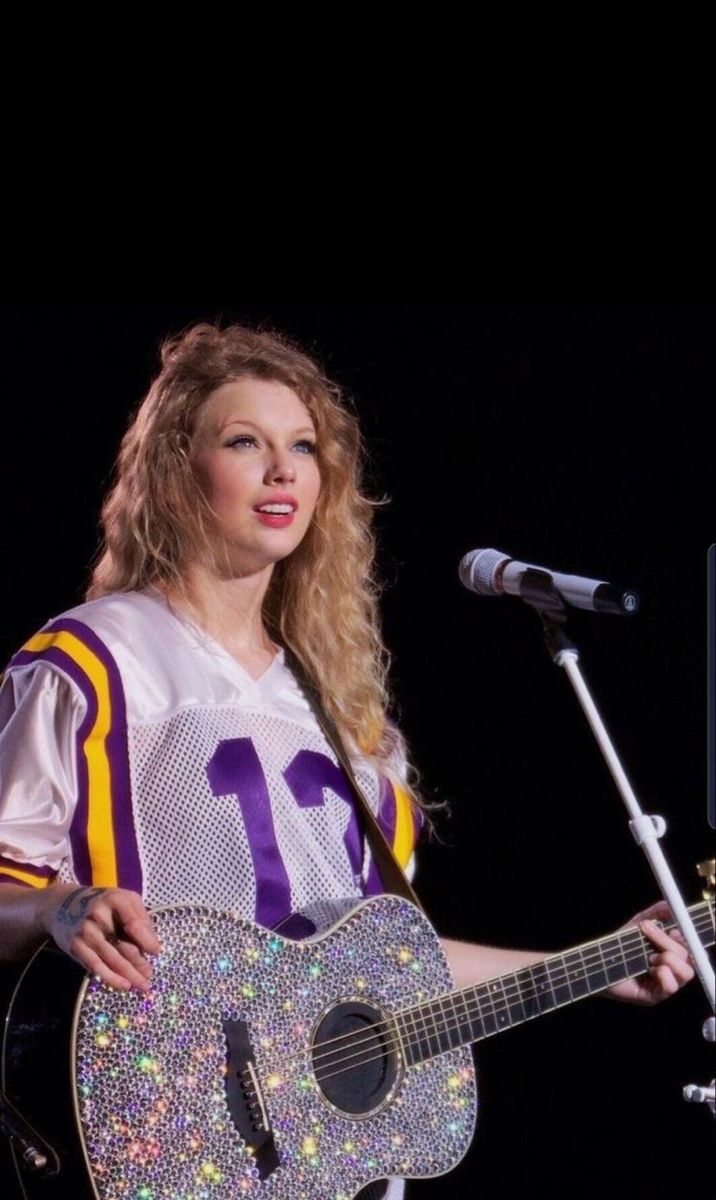 a woman holding a guitar while standing in front of a microphone