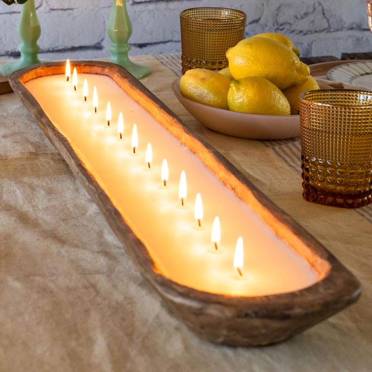 a long wooden table topped with lots of lit candles next to bowls of lemons