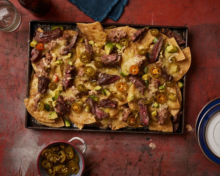 a tray filled with nachos and olives on top of a red table