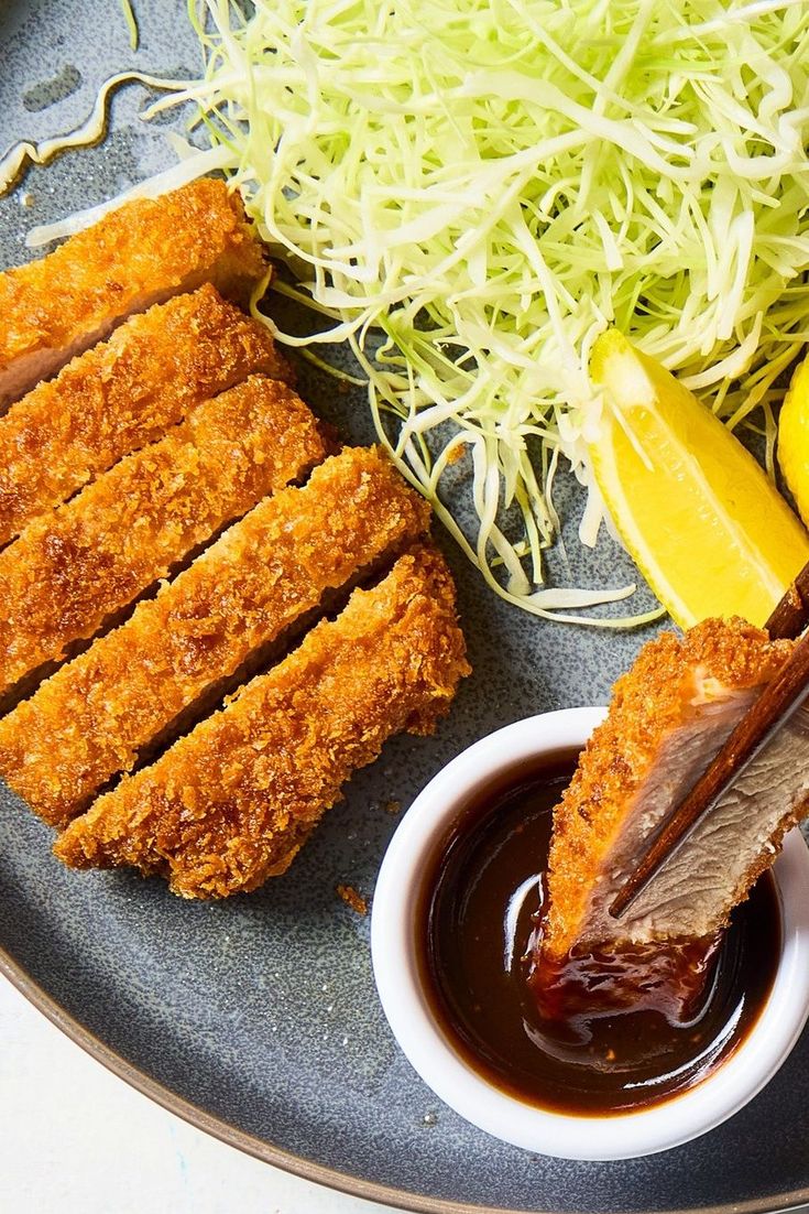 a plate with meat, vegetables and sauces on it next to a bowl of ketchup